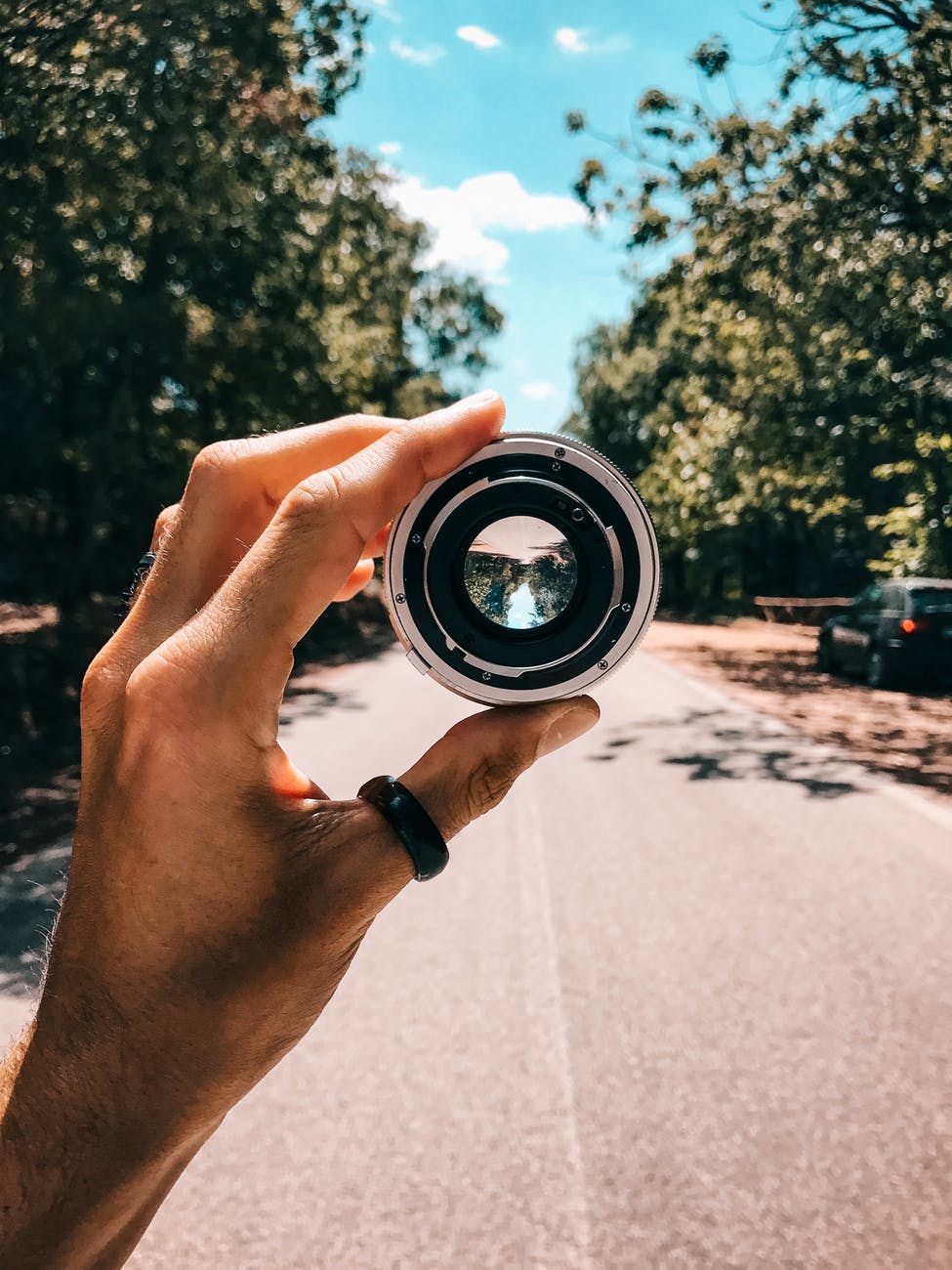 person holding camera lens in the middle of street under blue sky